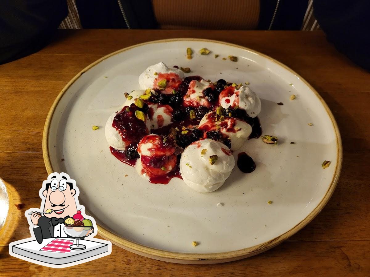 A plated berry and pistachio dessert at Tholoto with a Restaurant Guru illustration overlay